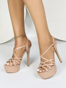 Close-up of nude patent leather platform sandals with crisscross straps and stiletto heels.