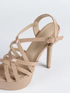 Detail of nude patent leather platform sandals with crisscross straps and stiletto heel.
