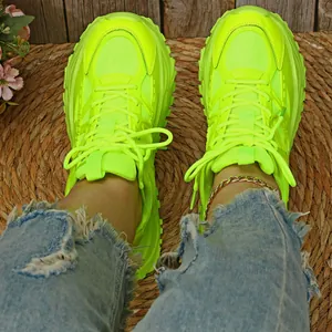 Detailweergave van neongele chunky dad sneakers gedragen met gerafelde jeans op een mat