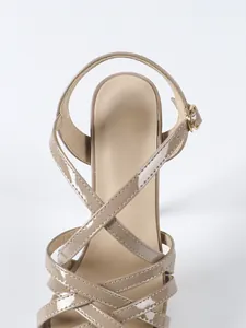 Close-up of khaki patent leather high-heeled sandals with elegant cross straps and buckle