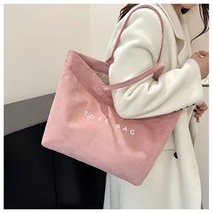 Gros plan sur un cabas en daim rose avec inscription blanche TOTE BAG porté par un mannequin