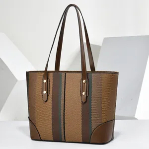 Detailed view of striped woven tote bag with brown leather handles and rivets.