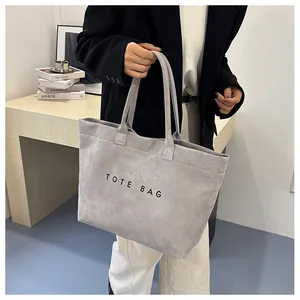 Détail du sac cabas en daim gris avec l'inscription TOTE BAG et une texture de cuir souple