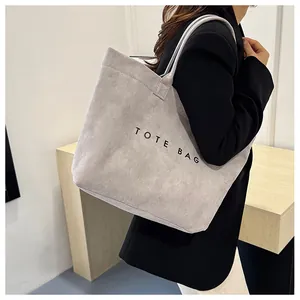 Vue détaillée d'un cabas en daim gris avec imprimé TOTE BAG porté par modèle
