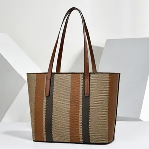Front view of a striped tote bag with brown leather handles on a minimalist background