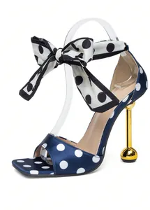 Detailweergave van marineblauwe polkadot sandaal met strik en gouden bolvormige hak