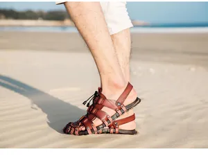 Side view of men's brown breathable leather beach sandals on a sunny beach sand