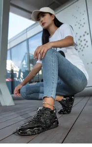 Detailed view of black sequined high-top casual sneakers worn by a model outdoors