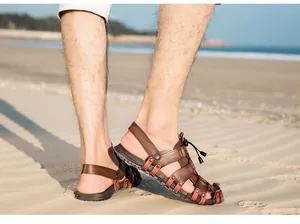 Detailed view of men's breathable leather beach sandals on sand with ocean background