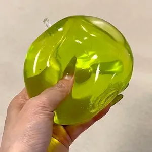 Nahaufnahme eines lichtdurchlässigen grünen Apfel-Maltose-Quetschspielzeugs in der Hand