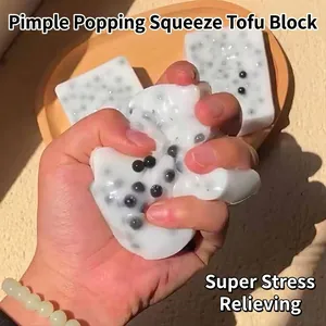 Main pressant un jouet anti-stress en forme de tofu blanc avec des perles noires
