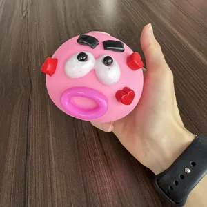 Hand holding a funny pink face squishy toy with red heart details for stress relief
