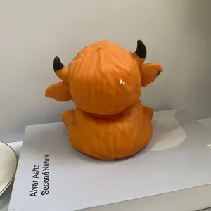 Detailed back view of orange Highland cow squishy toy with black horns on white box prop