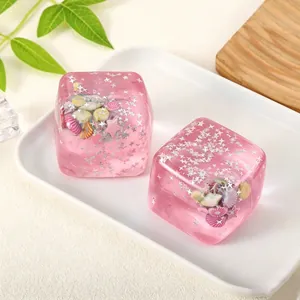 Detalle de conchas y purpurina de estrellas en cubo sensorial rosa translúcido.