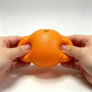 Close-up view of a realistic orange-shaped squeeze toy being compressed by human hands