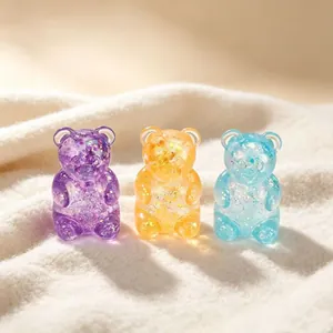 Close-up of translucent glitter bear toys in purple, orange and blue on soft fabric