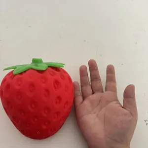 Detail view showing the jumbo size of the red strawberry squishy toy next to a hand