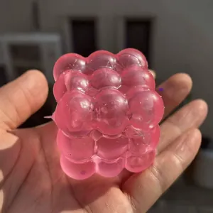 Zacht roze doorschijnend kubus-knijpspeeltje met glitters in hand tegen stress