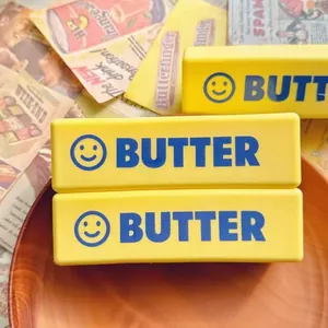 Nahaufnahme eines gelben Butter-Knautschspielzeugs mit Smiley und blauem Schriftzug.