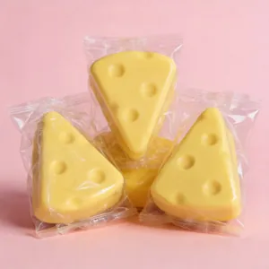 Nahaufnahme von drei einzeln verpackten Käse-Squishy-Spielzeugen auf einem rosa Hintergrund.