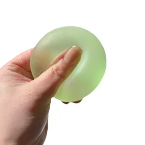 Translucent green maltose squishy stress relief toy ball being squeezed by hand on white background