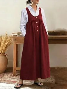 Casual loose red sleeveless pinafore dress with button details over a white shirt