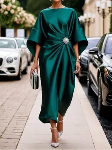 Detalle de un elegante vestido de satén verde esmeralda con broche floral brillante.