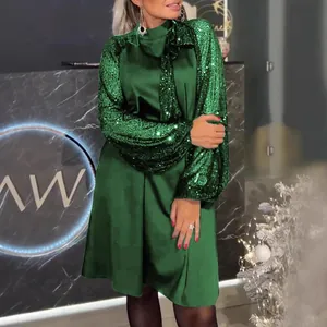 Dettaglio di mini abito in raso verde con maniche di paillettes e scollo a fiocco
