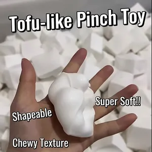 Soft white tofu block squishy stress relief toy being squeezed by hand in studio.