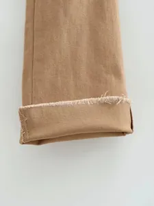 Dettaglio di jeans a zampa marroni che mostrano l'orlo a frange e la trama del twill