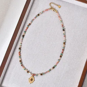 Nahaufnahme einer bunten Perlenkette mit goldenem Anhänger in einer Holzschale.