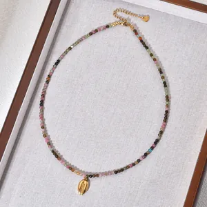 Elegante Detailaufnahme einer Halskette aus bunten Natursteinen mit goldenem Muschelanhänger