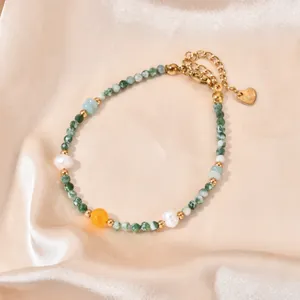 Detail of handmade beaded bracelet with green natural stones, pearls, and gold heart tag