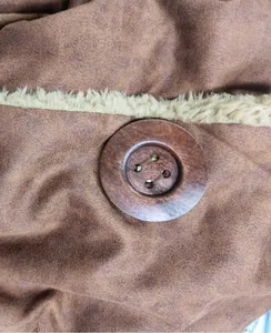 Détail d'un bouton en bois vintage sur une veste en daim avec une doublure peluche.