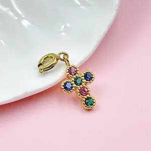 Detalle del colgante de cruz en acero dorado con piedras de colores y cierre de resorte.