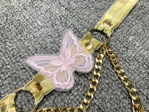 Dettaglio di farfalla rosa ricamata con catena dorata e borchie su accessorio top.