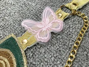 Dettaglio del ricamo a farfalla rosa e catena dorata sulla tracolla del top donna