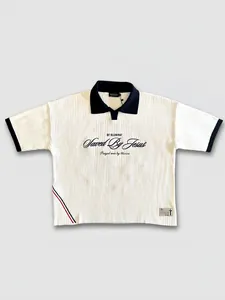 Détail du polo en maille plissée blanche avec broderie 'Saved By Jesus'