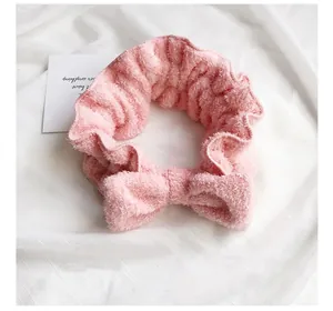 Primo piano di una fascia di peluche rosa con fiocco su sfondo di tessuto bianco.
