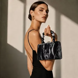 Détail montrant le motif de marbre noir et la poignée perlée du sac à main en acrylique.