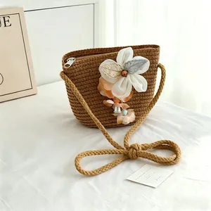Detailed shot of a woven straw crossbody bag with white flower charm on white surface