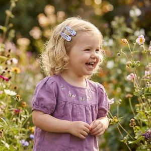 Close-up of a smiling little girl wearing colorful painted floral BB hair clips in a garden