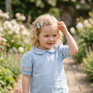 Cute rainbow pattern snap hair clips on young girl with blonde curls in sunny garden