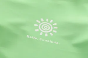 Close-up of the sun logo and Hello Sunshine text on green quick-dry swimwear fabric