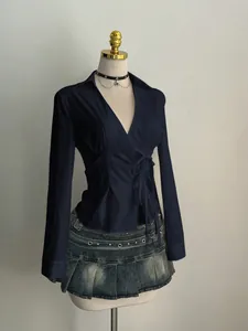 Elegant navy blue long-sleeve v-neck tie-waist blouse paired with distressed denim mini skirt