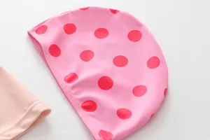 Close-up detail view of a pink girls' swimming cap featuring vibrant red polka dot patterns