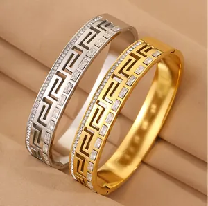 Close-up of gold and silver stainless steel bangles with Greek key crystal patterns.