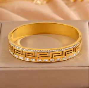 Detailed view of gold-plated stainless steel bangle with meander pattern and crystals