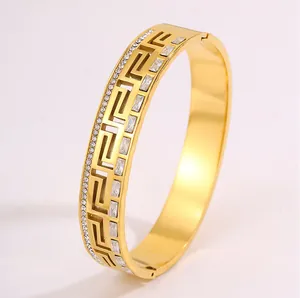 Macro view of gold stainless steel bangle with Greek key pattern and rhinestone inlay