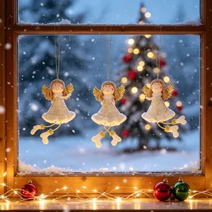 Drie schattige engelornamenten hangend voor een besneeuwd raam met kerstverlichting.